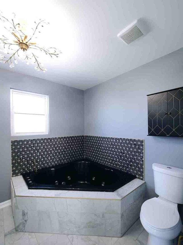 full bathroom featuring toilet, a whirlpool tub, marble look tiles, and baseboards