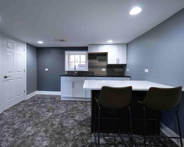 kitchen featuring a sink, white cabinets, baseboards, a breakfast bar, and recessed lighting