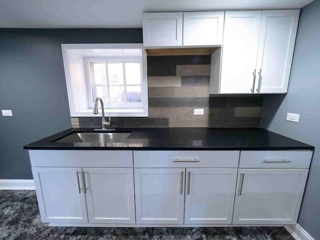 kitchen featuring a sink, white cabinetry, tasteful backsplash, dark countertops, and baseboards
