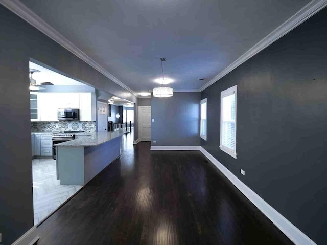 kitchen featuring appliances with stainless steel finishes, a peninsula, white cabinetry, ornamental molding, and baseboards