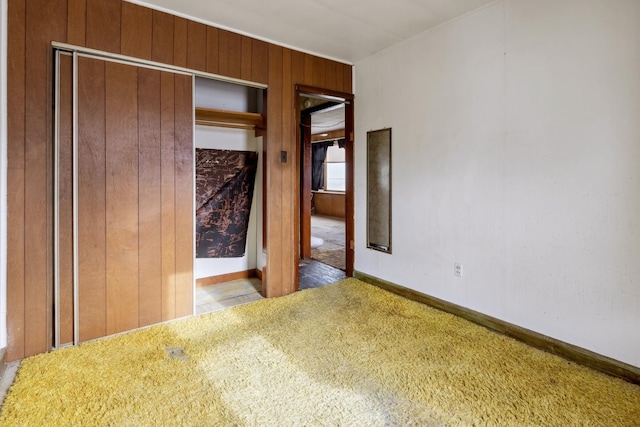 empty room featuring carpet floors, wooden walls, and baseboards