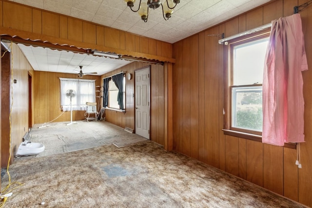 unfurnished room with healthy amount of natural light, carpet, wood walls, a chandelier, and a ceiling fan