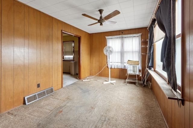 empty room featuring carpet flooring, a ceiling fan, and wood walls