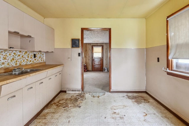 kitchen featuring a sink, light countertops, white cabinets, backsplash, and baseboards