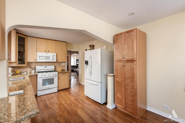 kitchen featuring white appliances, a sink, arched walkways, light wood finished floors, and tasteful backsplash