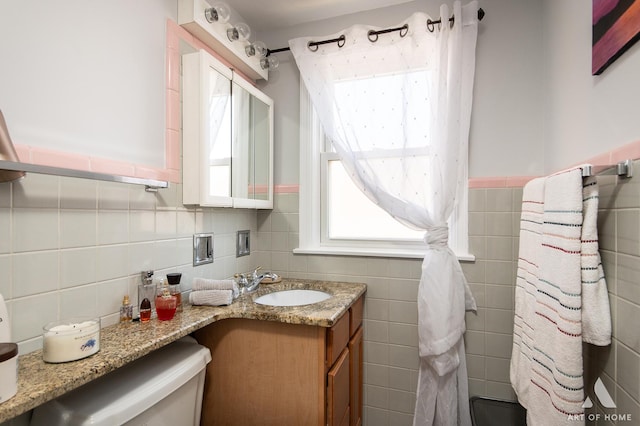 bathroom featuring tile walls, toilet, vanity, and wainscoting