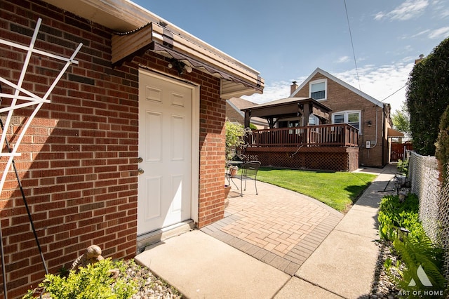 property entrance featuring brick siding, a patio, and a wooden deck