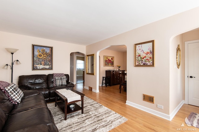 living area featuring arched walkways, light wood-style flooring, and baseboards
