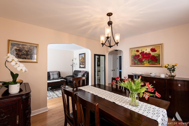 dining room featuring arched walkways, wood finished floors, a chandelier, and baseboards