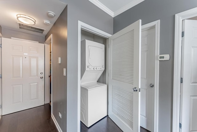 laundry area with stacked washer / drying machine, crown molding, baseboards, and dark wood-type flooring