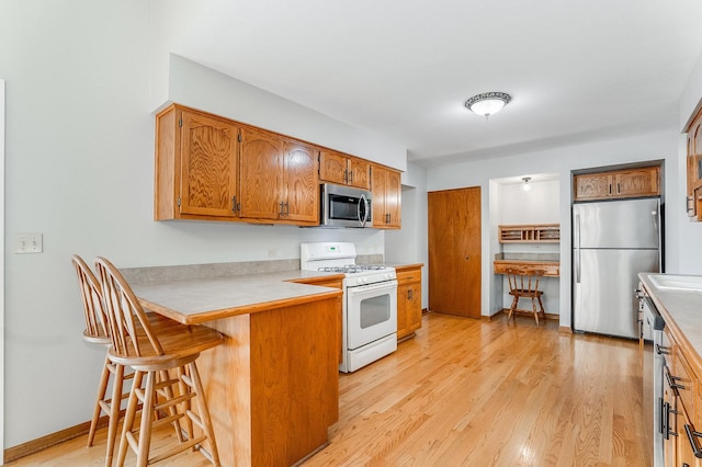 1936 Sybil Dr, Crest Hill, IL 60403 - kitchen featuring appliances with stainless steel finishes, a peninsula, light wood-type flooring, brown cabinets, and a breakfast bar
