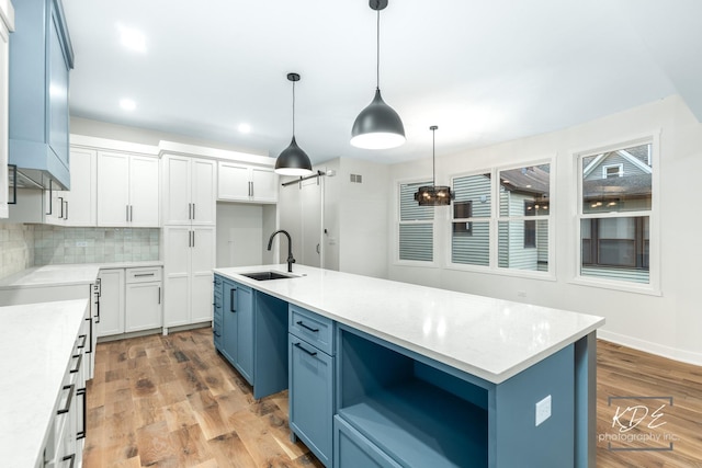 715 N Brainard St, Naperville, IL 60563 - kitchen with blue cabinets, an island with sink, backsplash, light wood finished floors, and white cabinetry