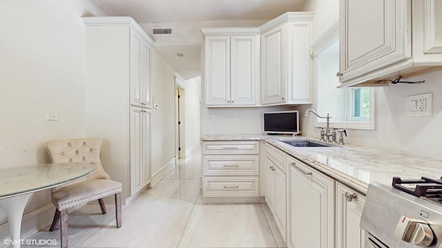 kitchen with a sink, light stone countertops, white cabinetry, and stove