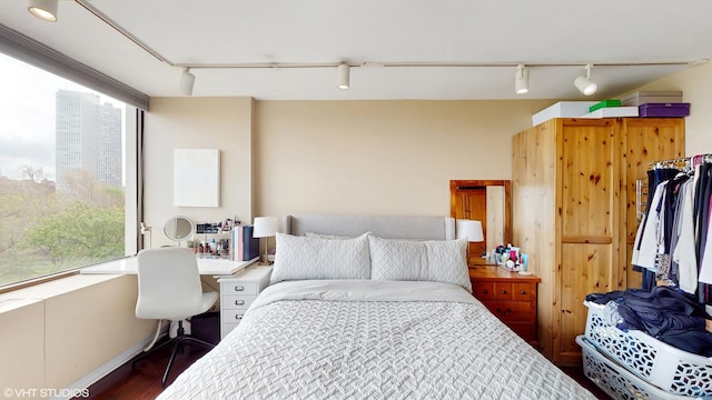 bedroom with rail lighting, wood finished floors, and an office area