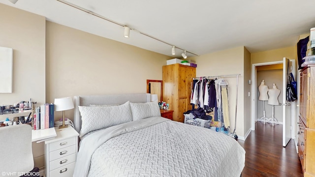 bedroom featuring a closet, dark wood-type flooring, track lighting, and baseboards