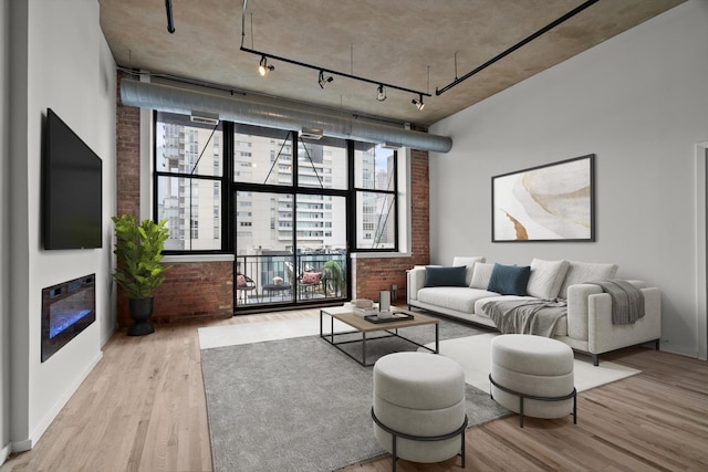 living room with brick wall, wood finished floors, rail lighting, and a glass covered fireplace