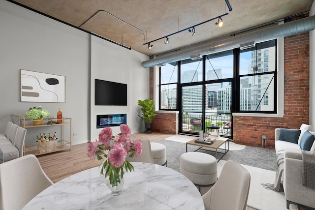 living room featuring brick wall, a glass covered fireplace, rail lighting, and wood finished floors