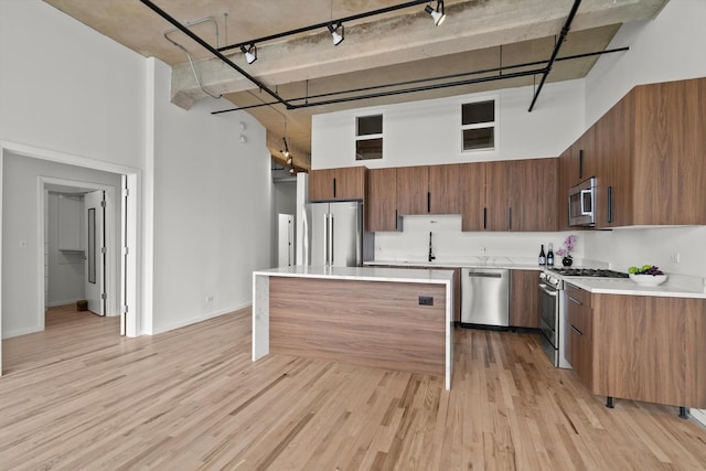 kitchen featuring appliances with stainless steel finishes, a high ceiling, light countertops, a center island, and light wood-type flooring