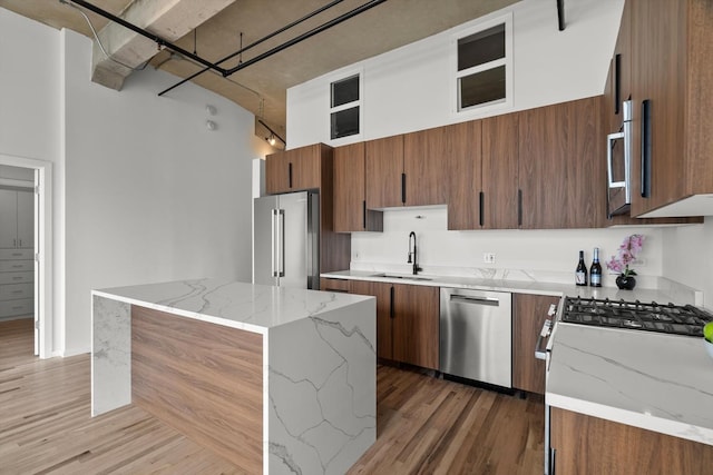 kitchen with stainless steel appliances, a sink, light wood finished floors, brown cabinetry, and a towering ceiling