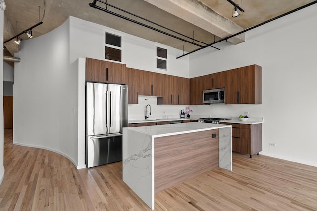 kitchen featuring stainless steel appliances, rail lighting, a towering ceiling, modern cabinets, and a sink