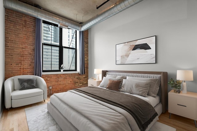 bedroom featuring brick wall and wood finished floors