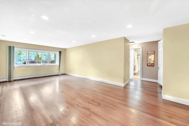 empty room featuring baseboard heating, light wood-type flooring, baseboards, and recessed lighting