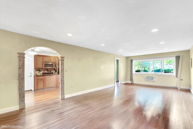 spare room featuring arched walkways, light wood finished floors, baseboards, recessed lighting, and a wall unit AC