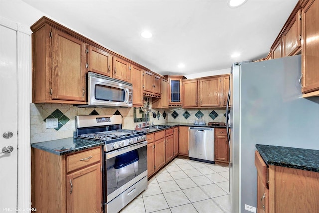 kitchen with appliances with stainless steel finishes, a sink, brown cabinetry, decorative backsplash, and light tile patterned floors