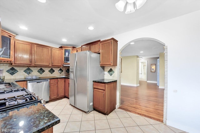 kitchen with appliances with stainless steel finishes, arched walkways, backsplash, brown cabinets, and recessed lighting