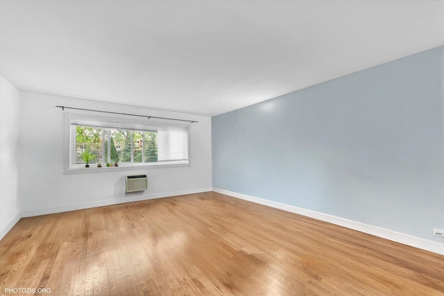 empty room with a wall mounted AC, light wood-style floors, and baseboards