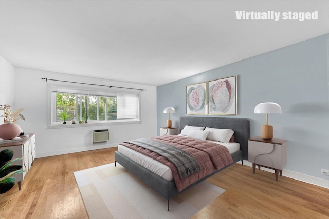 bedroom with an AC wall unit, light wood-style flooring, and baseboards