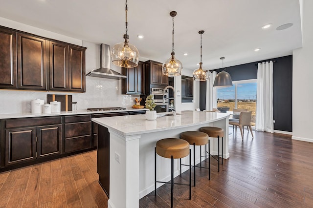 1995 Norwich Ln, Bolingbrook, IL 60490 - kitchen featuring wall chimney range hood, decorative backsplash, a kitchen bar, an island with sink, and recessed lighting