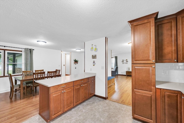 2908 Rolling Acres Dr, Champaign, IL 61822 - kitchen with light countertops, a peninsula, brown cabinetry, a textured ceiling, and backsplash