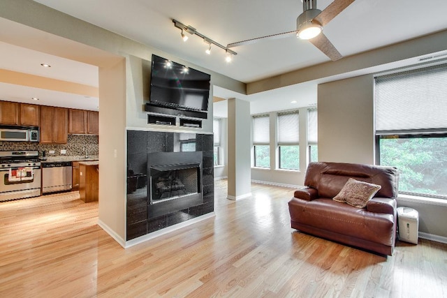 living area with light wood-type flooring, a ceiling fan, track lighting, a fireplace, and baseboards