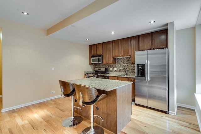 kitchen featuring appliances with stainless steel finishes, decorative backsplash, a kitchen island, light wood-style floors, and light stone counters