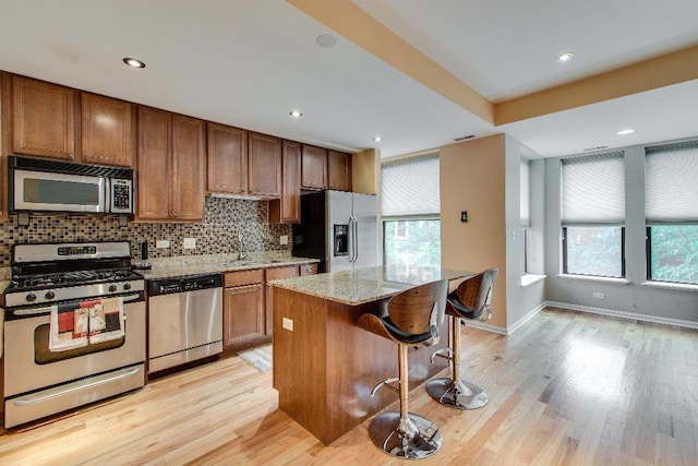kitchen with stainless steel appliances, decorative backsplash, light wood finished floors, light stone counters, and a sink