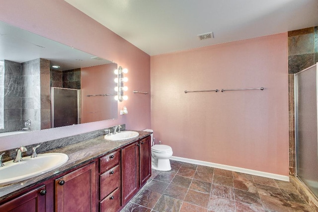full bathroom featuring a shower stall, baseboards, double vanity, toilet, and stone finish floors