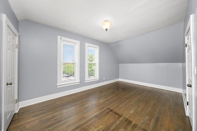 additional living space featuring vaulted ceiling, dark wood-type flooring, and baseboards