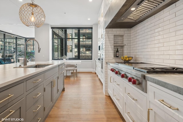 1109 W Washington Blvd Unit 2B, Chicago, IL 60607 - kitchen with a sink, wall chimney range hood, stainless steel gas stovetop, light countertops, and backsplash