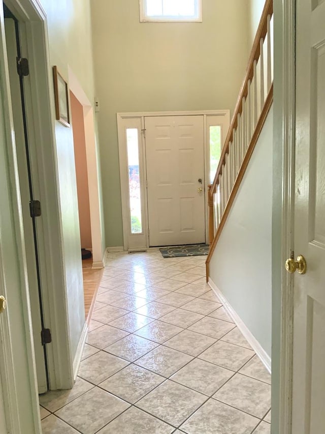 foyer entrance with a towering ceiling, light tile patterned floors, stairs, and baseboards