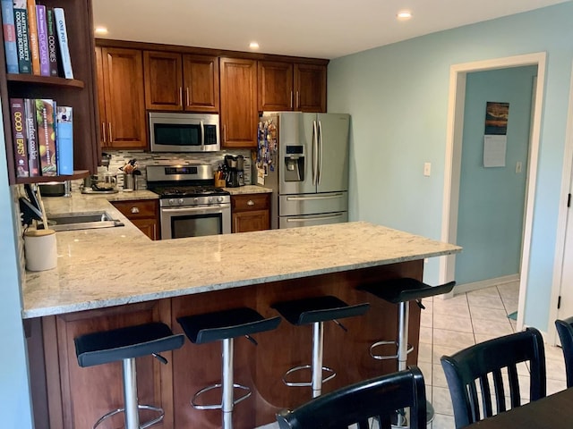 kitchen with stainless steel appliances, light stone countertops, a peninsula, tasteful backsplash, and light tile patterned flooring