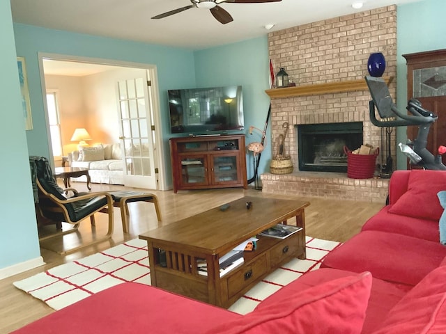 living area with a fireplace, ceiling fan, and wood finished floors