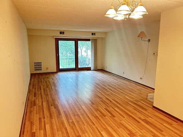 spare room featuring a chandelier, light wood finished floors, and baseboards