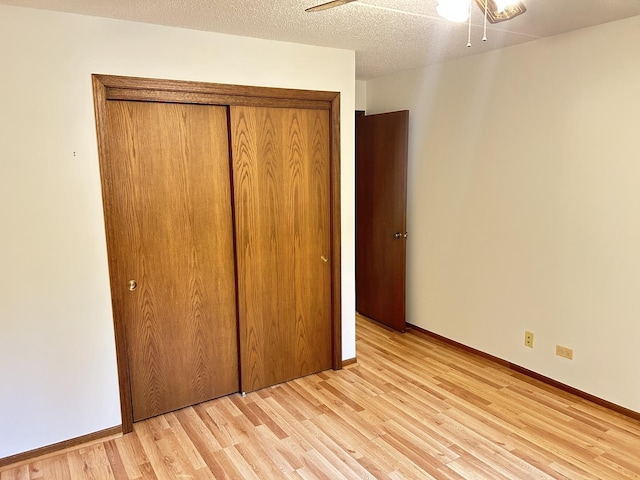 unfurnished bedroom with light wood-type flooring, a closet, baseboards, and a textured ceiling