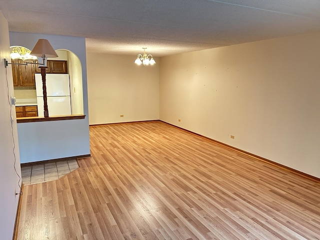 unfurnished living room featuring light wood-style floors, a chandelier, and baseboards