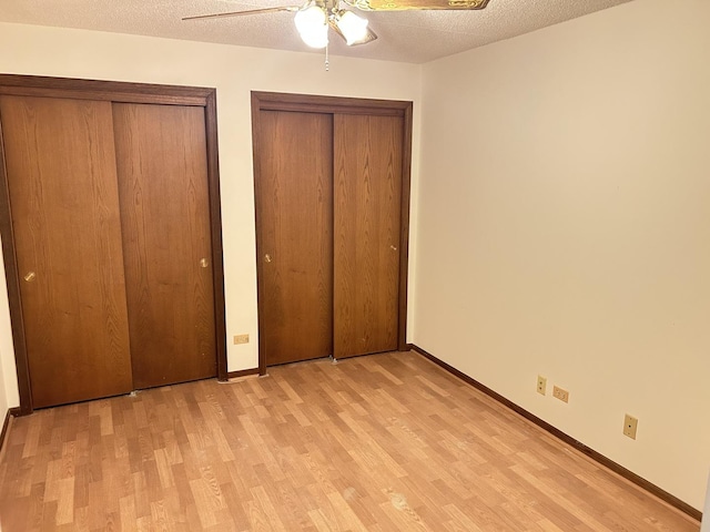unfurnished bedroom with two closets, light wood-type flooring, baseboards, and a textured ceiling