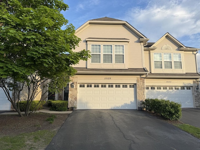 view of front facade featuring an attached garage, asphalt driveway, and stone siding