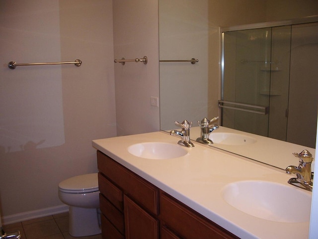 bathroom with tile patterned flooring, toilet, double vanity, a shower with door, and baseboards