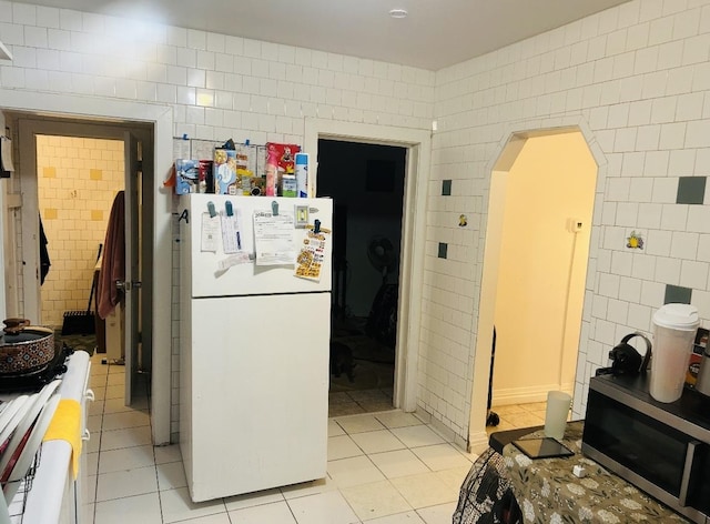 kitchen with white appliances, tile walls, light tile patterned floors, and arched walkways