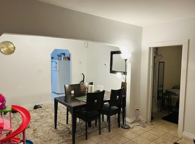 dining space with arched walkways, light tile patterned flooring, and baseboards
